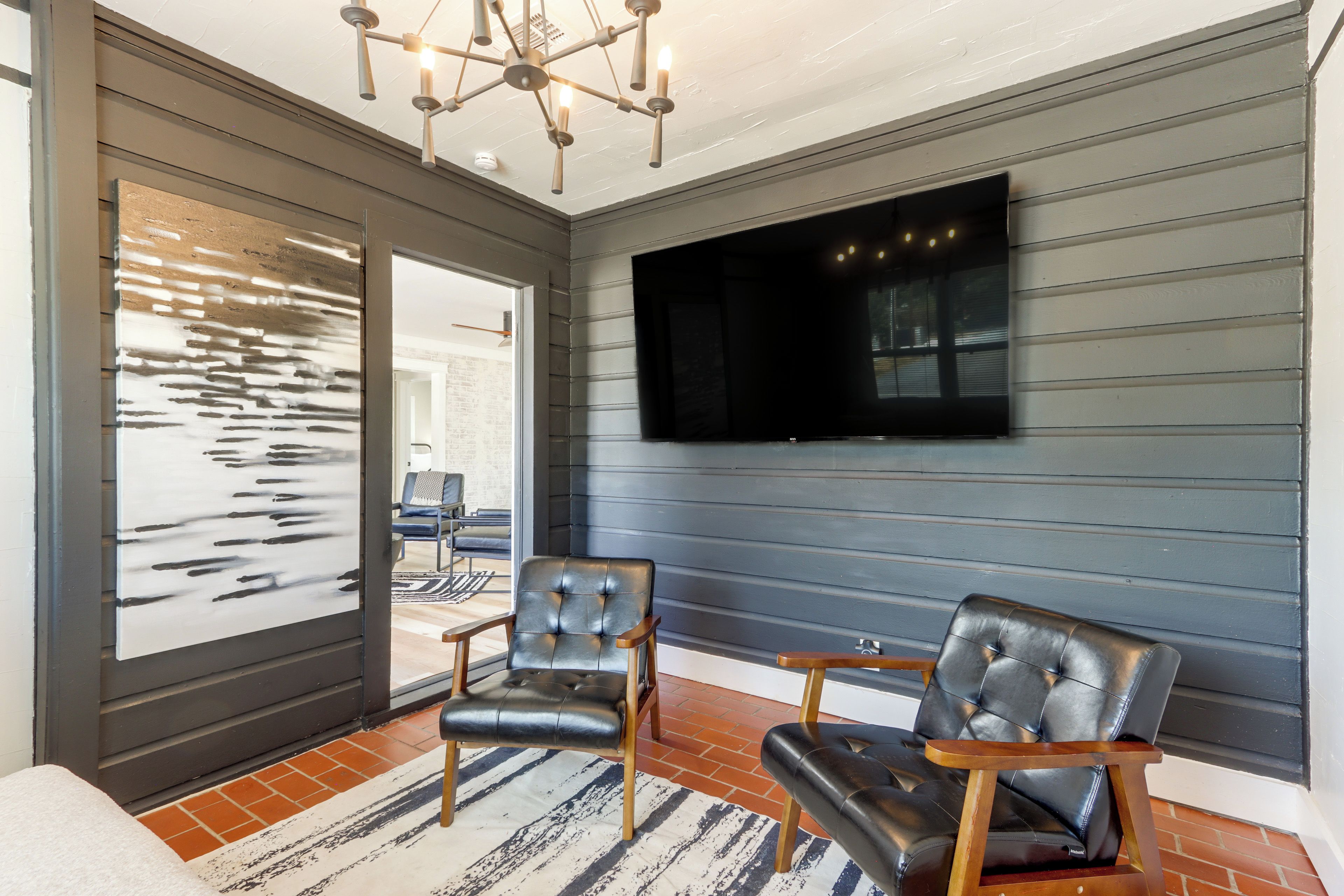 A modern living room with a large flat-screen TV mounted on a dark wall, two leather armchairs, a patterned rug, and a ceiling light fixture.