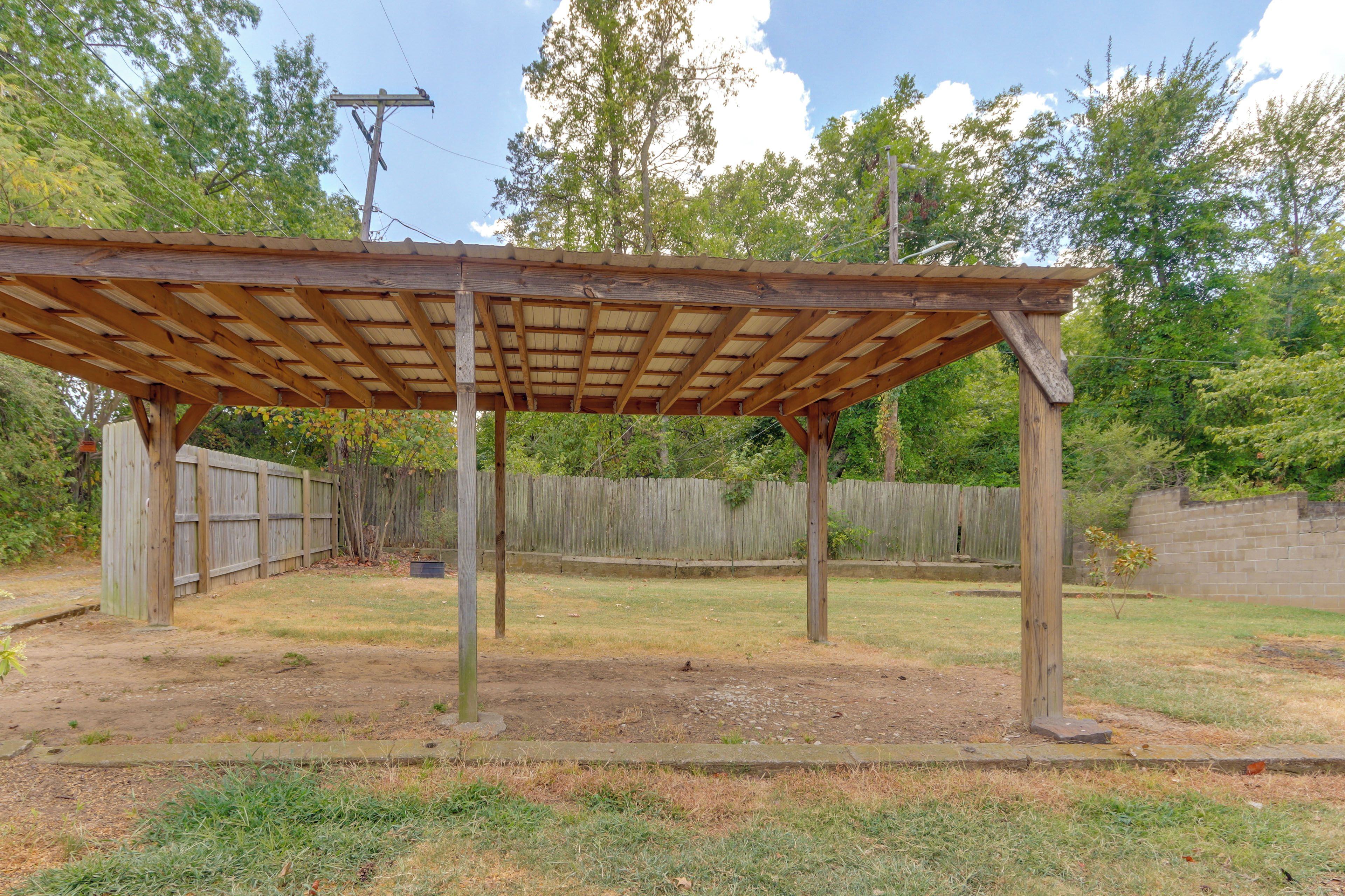 A wooden pergola structure in a backyard with a wooden fence in the background.