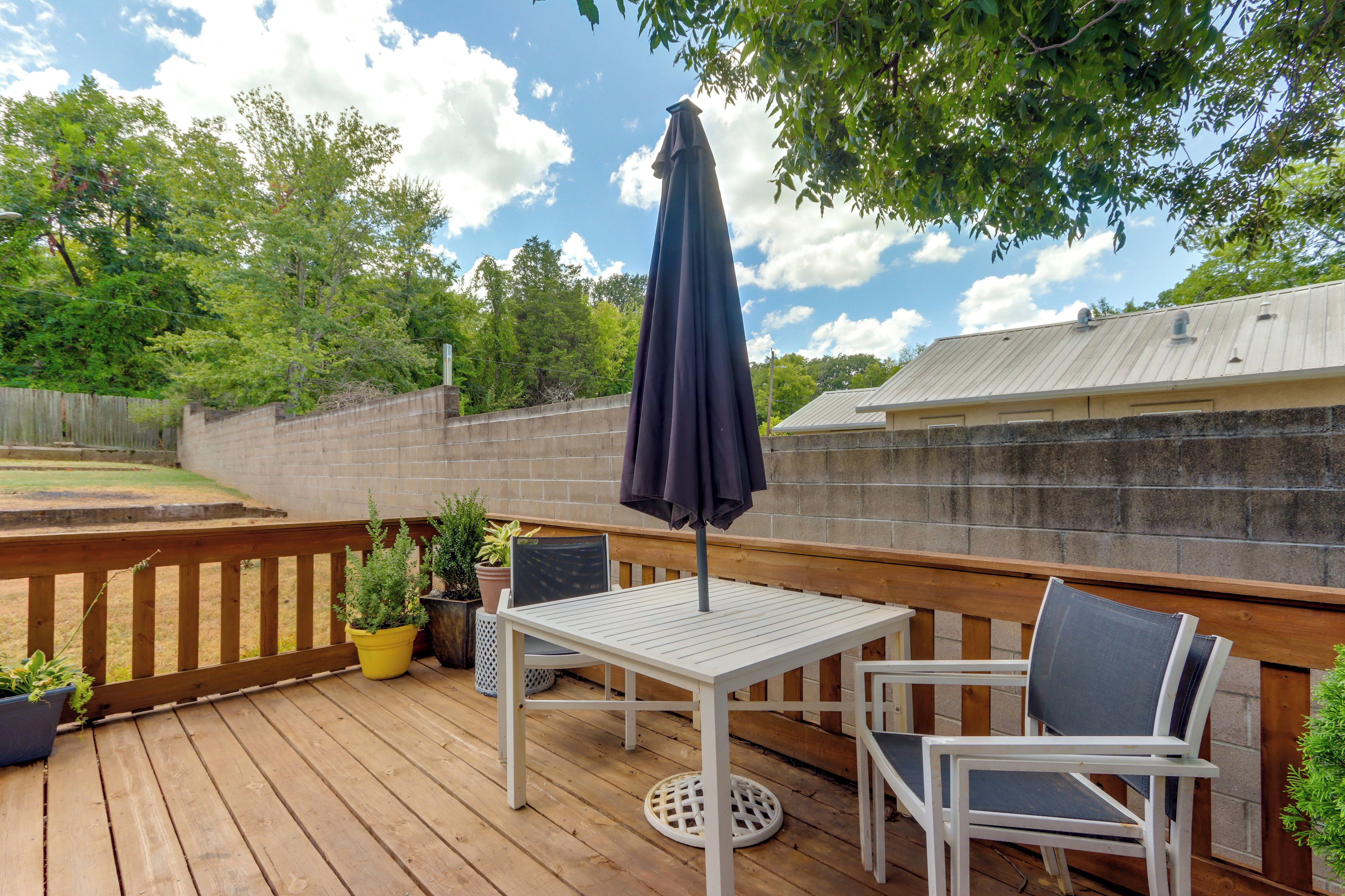 A wooden deck with a table and chairs, a potted plant, and a black umbrella.