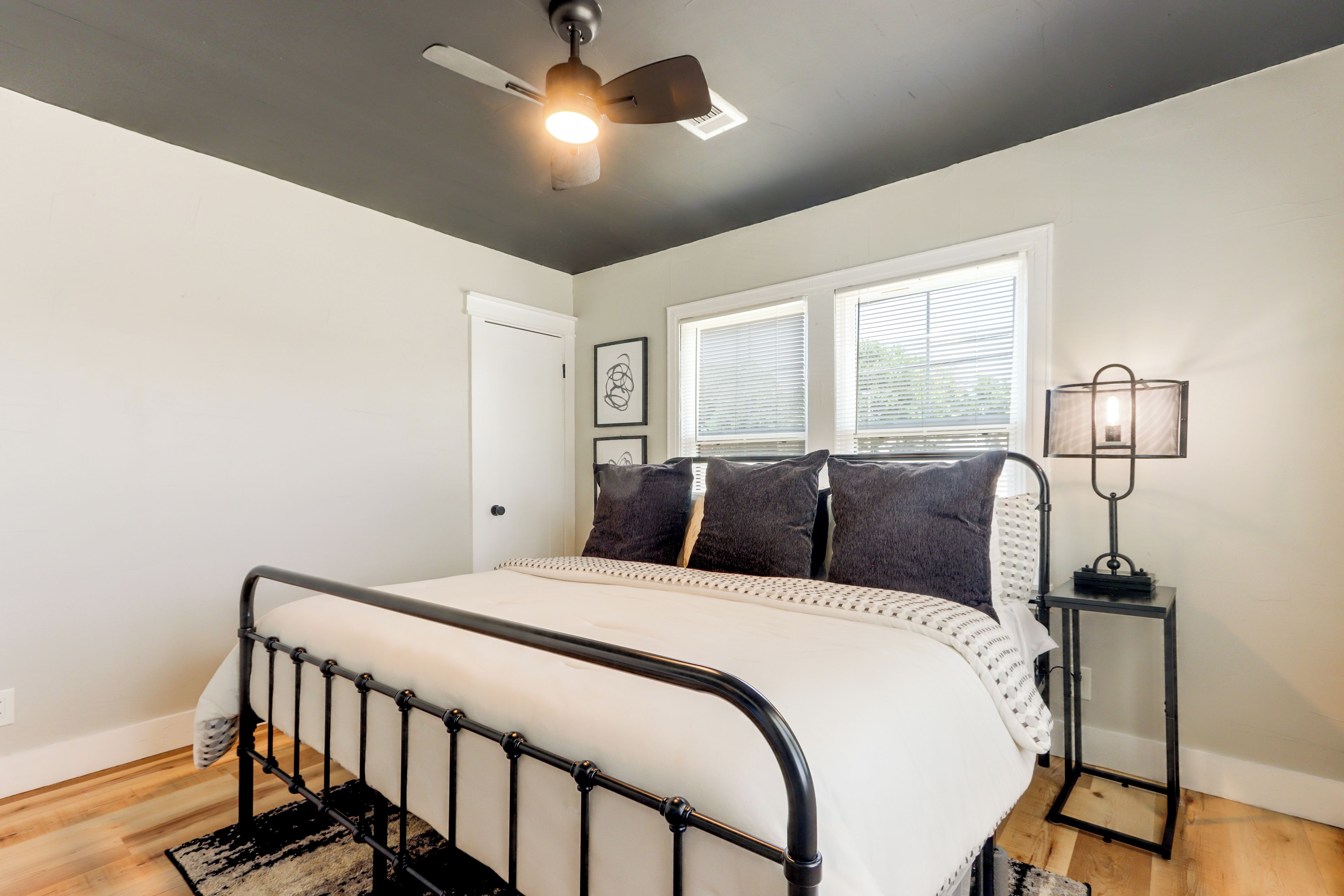 A bedroom with a bed, a ceiling fan, a window with blinds, and a bedside table with a lamp.