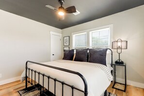 Ein Schlafzimmer mit einem Bett, einem Deckenventilator, einem Fenster mit Jalousien und einem Nachttisch mit einer Lampe.