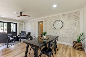 A modern living room with a dark wooden dining table, black chairs, a black sofa, and a brick-patterned wall.