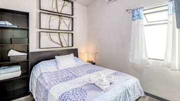 A neatly made bed with a blue and white patterned bedspread, a headboard, and a bedside table with a lamp.