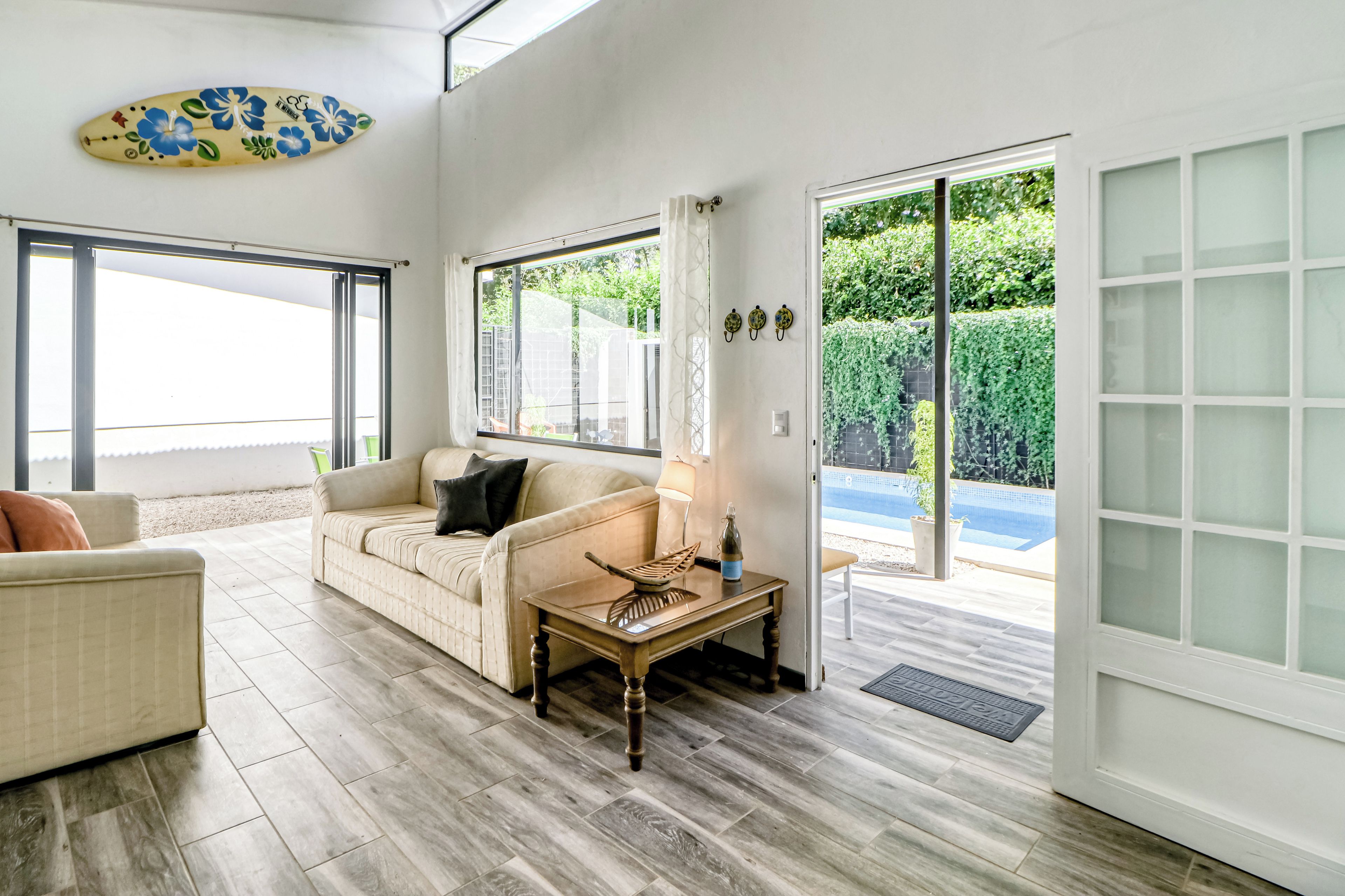 Amplia sala de estar con sofá, una mesa de centro y vista a una piscina a través de puertas correderas de cristal.