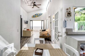 A modern interior with a dining area, sofas, a ceiling fan, and a view through a glass door.