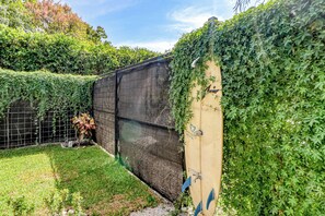 A fenced outdoor area with a grassy lawn, a small tree, and a wall with a logo.