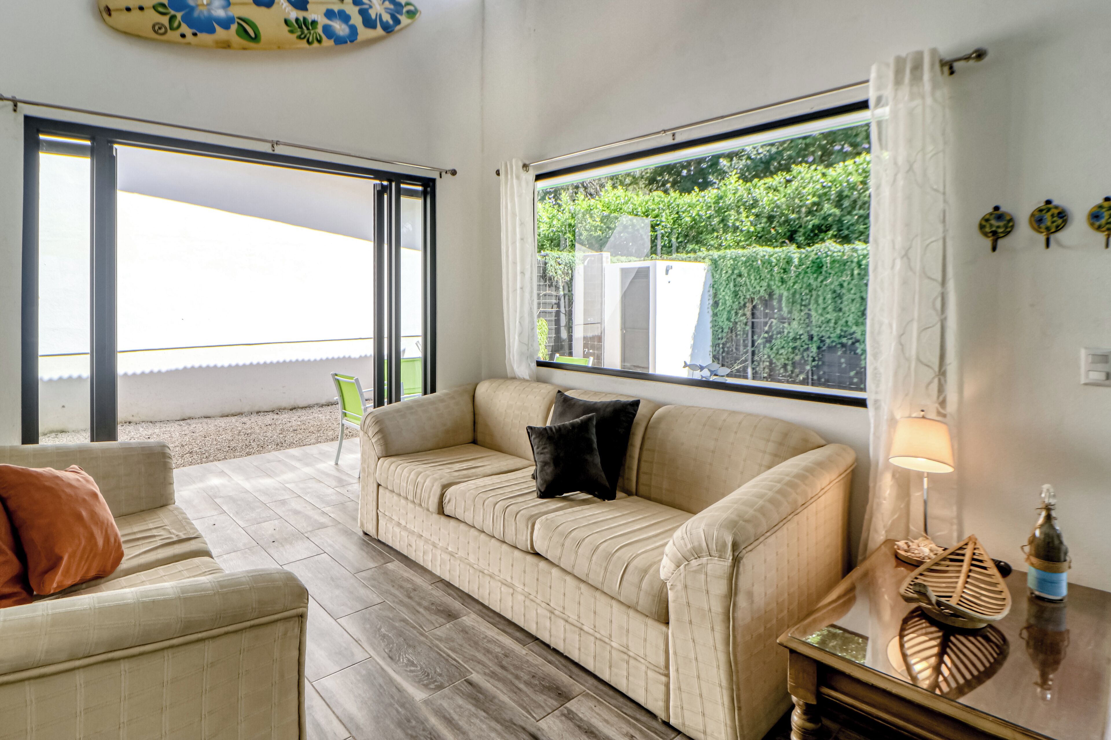 A living room with a beige sofa, a green chair, a wooden coffee table, and a window with a view of greenery.