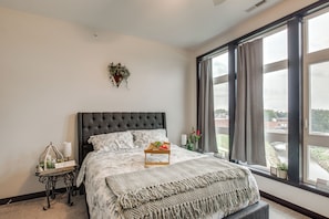 A bedroom with a large bed, a bedside table, a window with curtains, and a wall-mounted plant. - Rooftop Deck, Great Views! Modern Condo Near Dtwn (Dyersville)