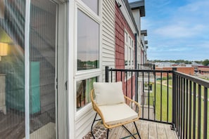 A balcony with a wicker chair, a view of the neighborhood, and a building with red siding.