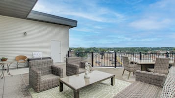 A covered patio with wicker furniture, a welcome sign, and a view of the city.