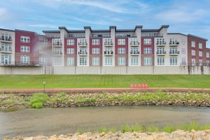 A multi-story residential building with a stone facade, a grassy area in front, and a small body of water.