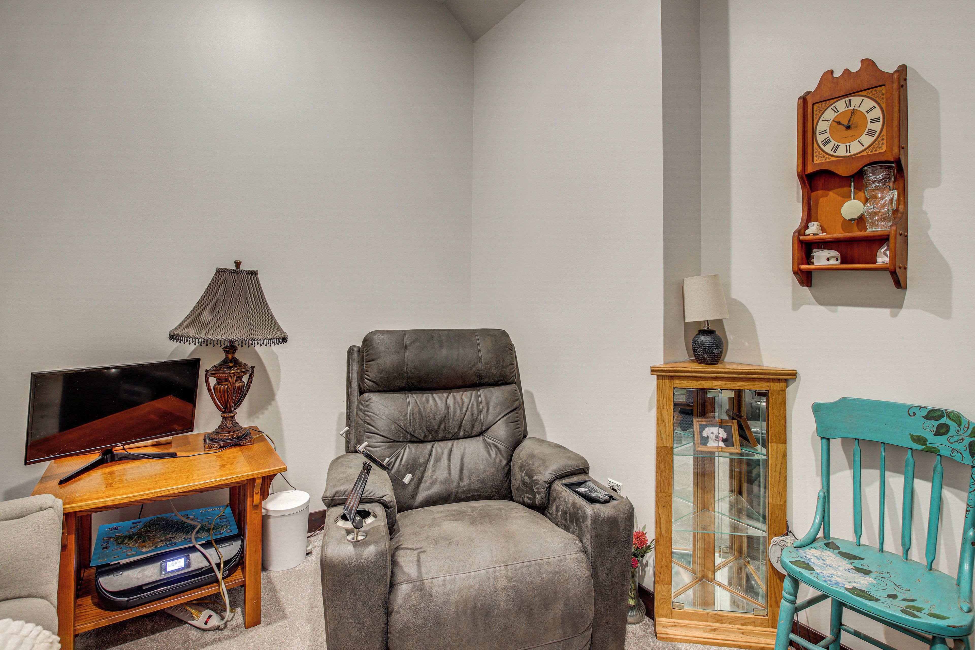 A living room with a leather armchair, a television, a lamp, a clock, and a small cabinet.