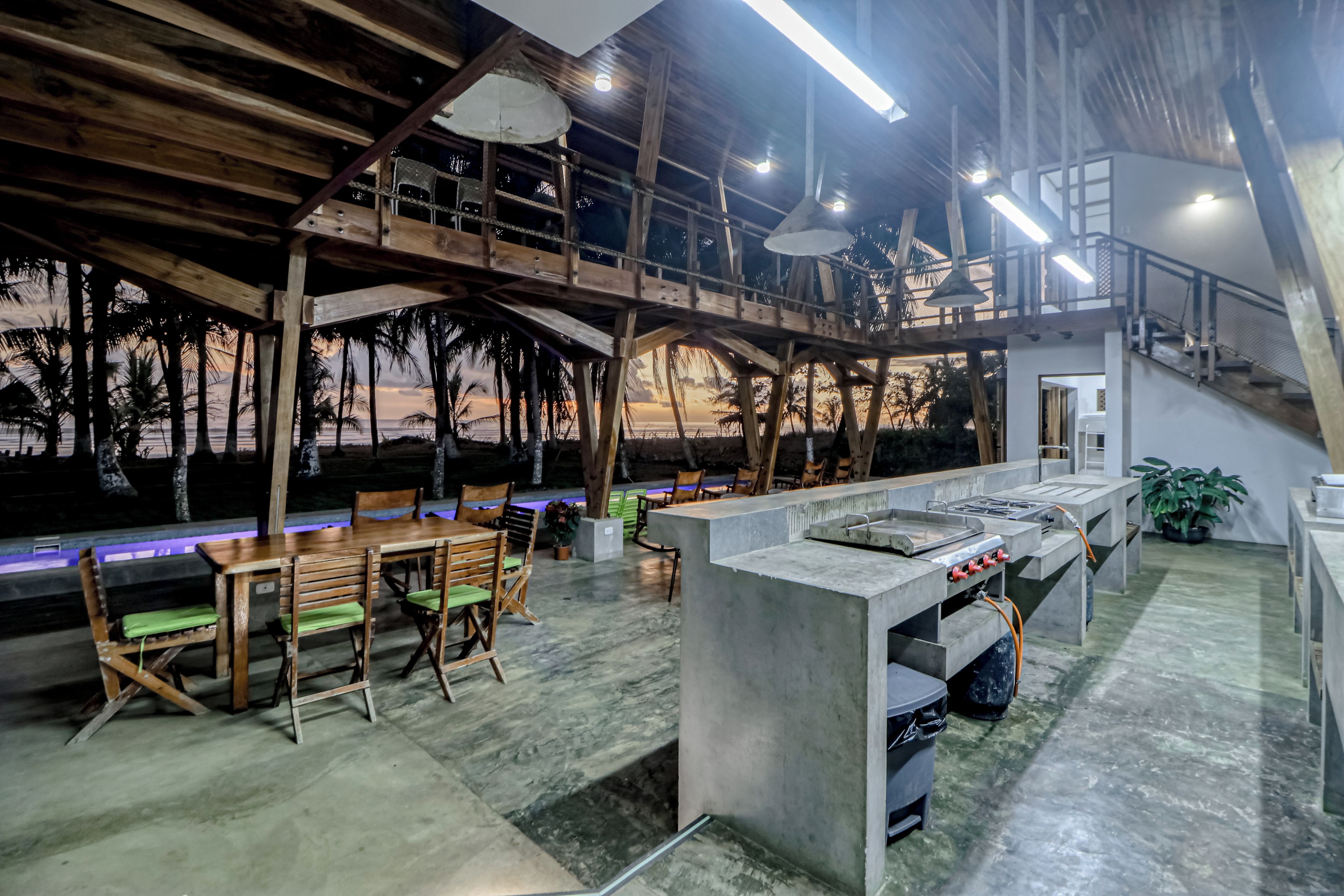 An indoor bar area with a high ceiling, wooden beams, and a view of palm trees and the ocean.