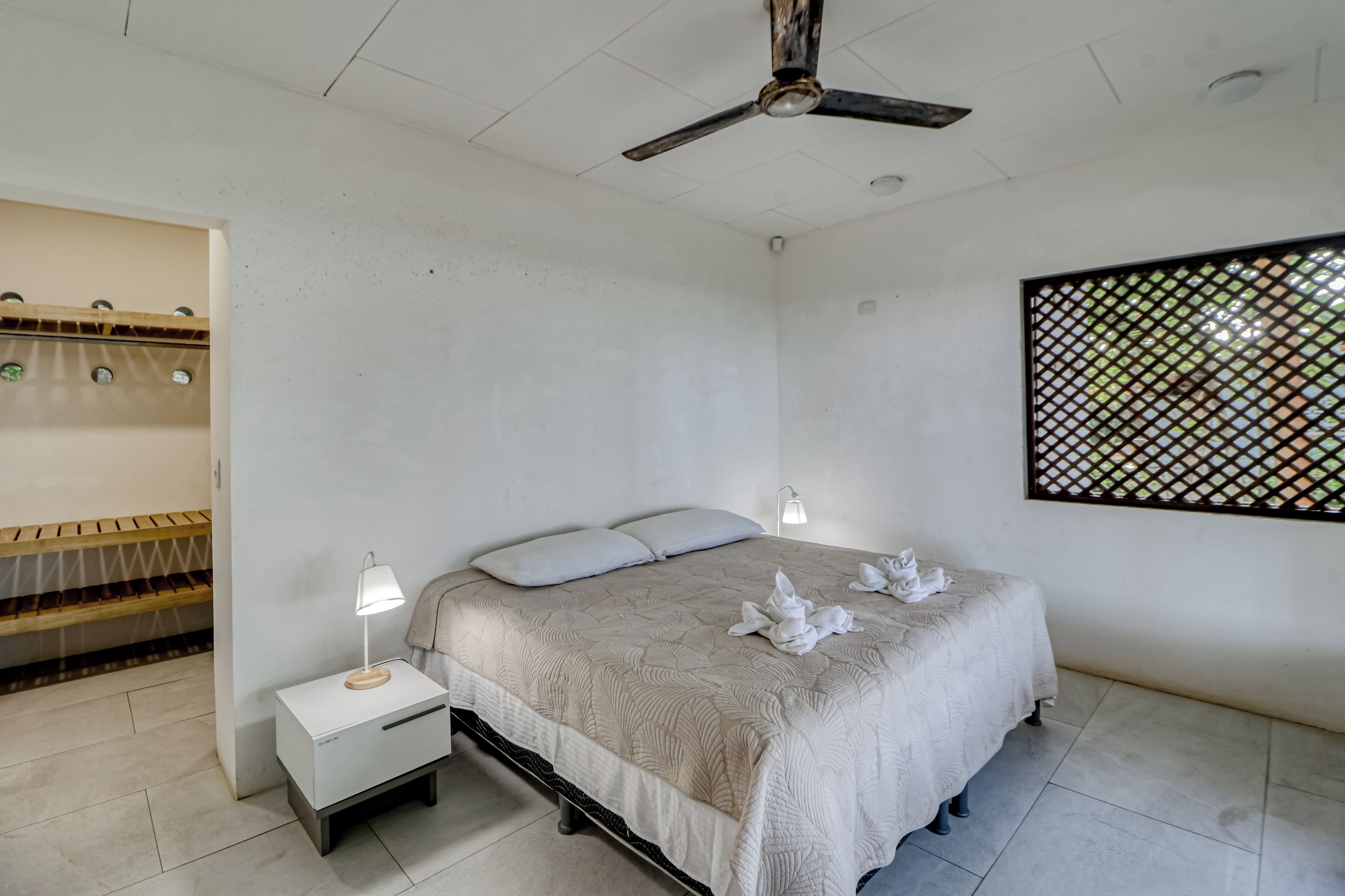 A bedroom with a bed, bedside tables, a ceiling fan, and a window with a view.