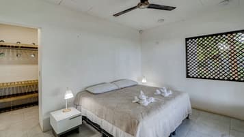 A bedroom with a bed, bedside tables, a ceiling fan, and a window with a view.