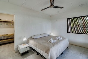 A bedroom with a bed, bedside tables, a ceiling fan, and a window with a view.
