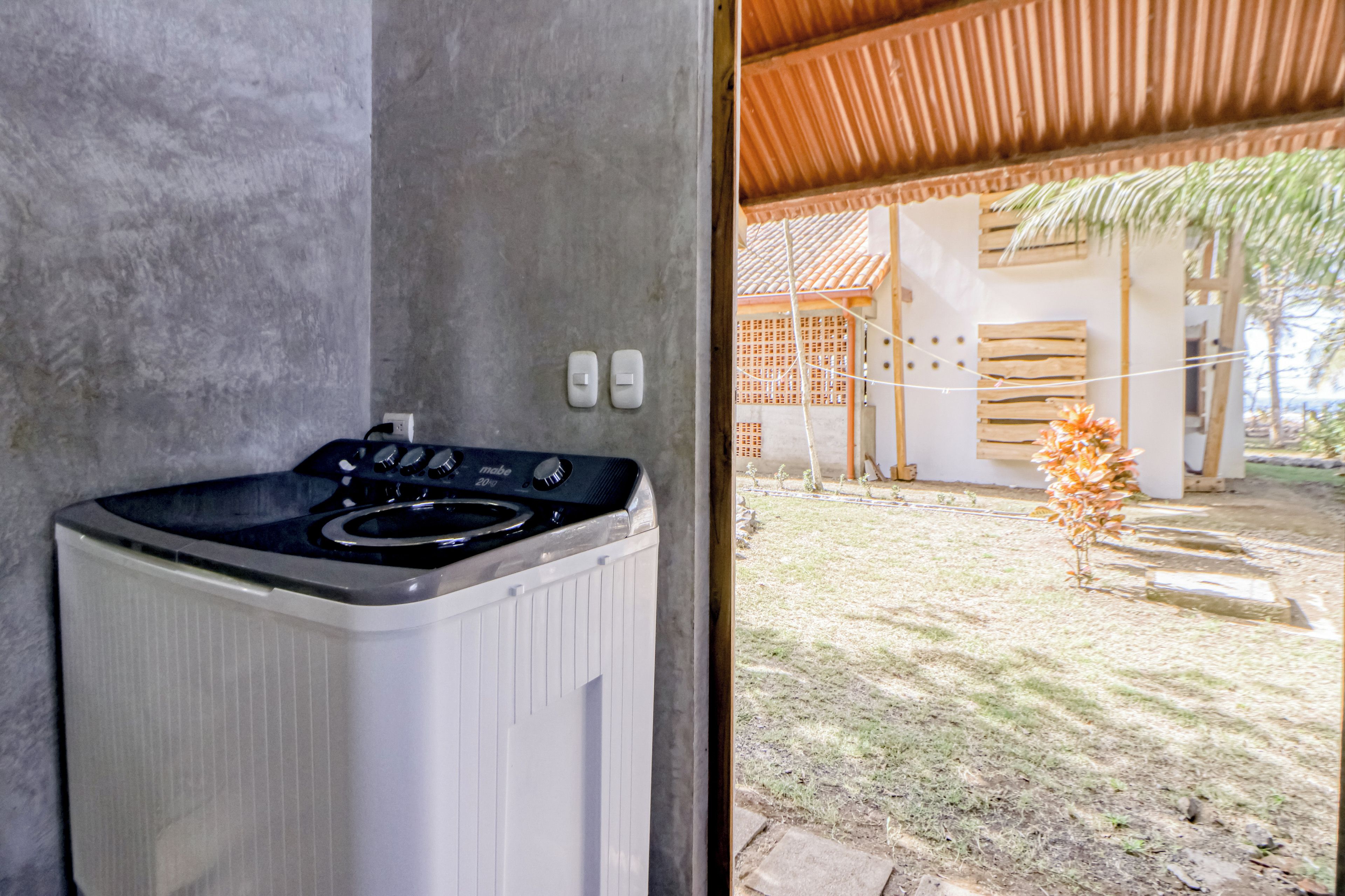 Une cuisine moderne dotée d’une cuisinière intégrée et offrant une vue sur un espace extérieur abrité, avec une structure en bois et un petit arbre.