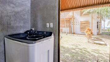 Une cuisine moderne dotée d’une cuisinière intégrée et offrant une vue sur un espace extérieur abrité, avec une structure en bois et un petit arbre.