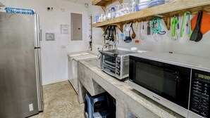 A kitchen with a stainless steel refrigerator, a microwave, and a toaster oven. There are shelves above the counter holding dishes and utensils.