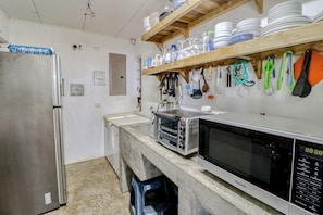 A kitchen with a stainless steel refrigerator, a microwave, and a toaster oven. There are shelves above the counter holding dishes and utensils.