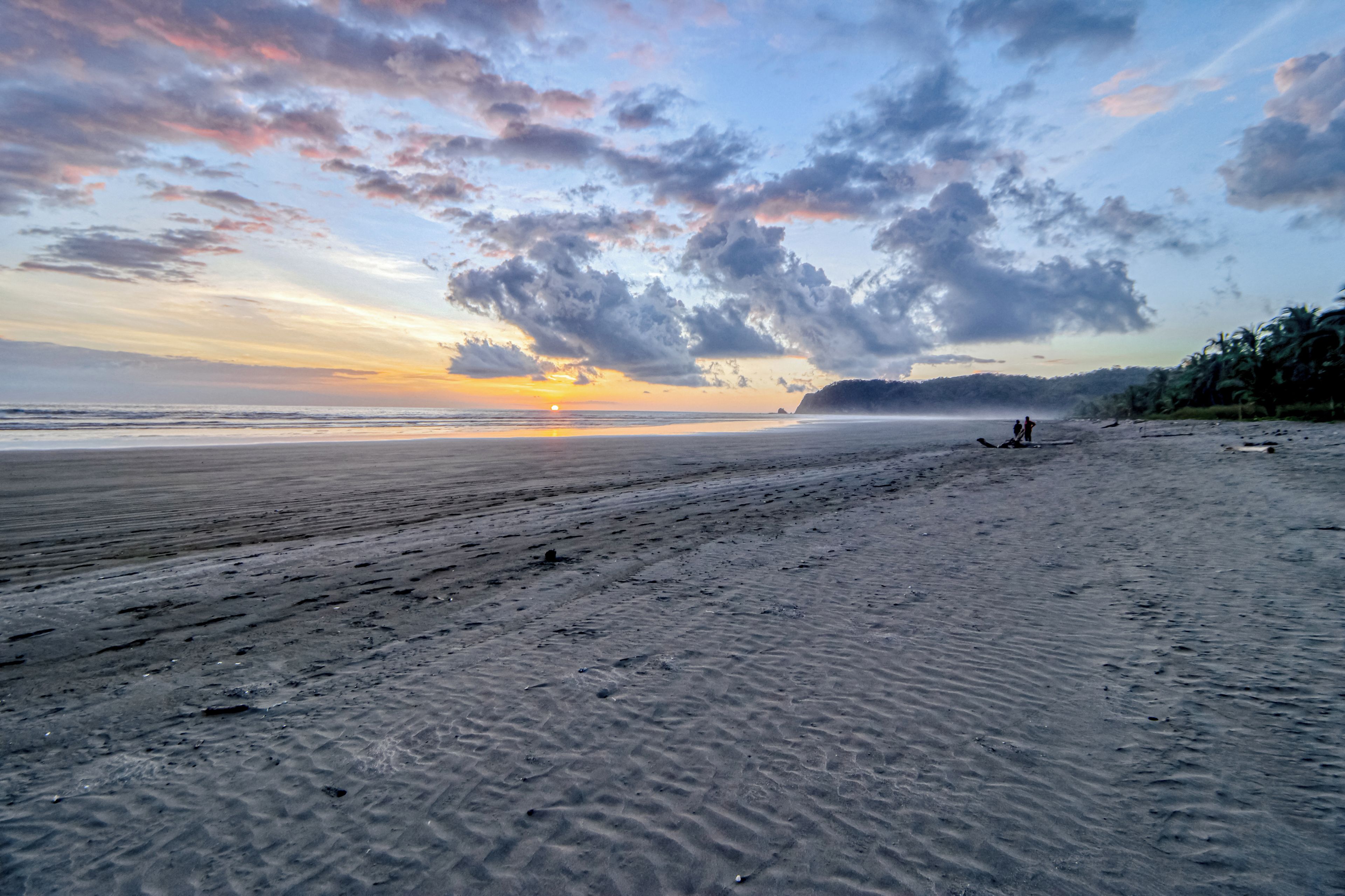 A beach with a sunset, a distant shoreline, and a few people.
