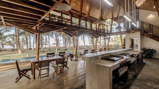 A spacious kitchen with a long counter, wooden chairs, and a view of the outdoors.
