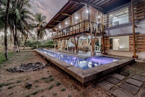 A modern house with a pool, outdoor furniture, and palm trees.