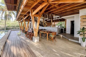 Una terraza exterior de madera con piscina, mobiliario de madera y un espacio cubierto con vistas al paisaje circundante.