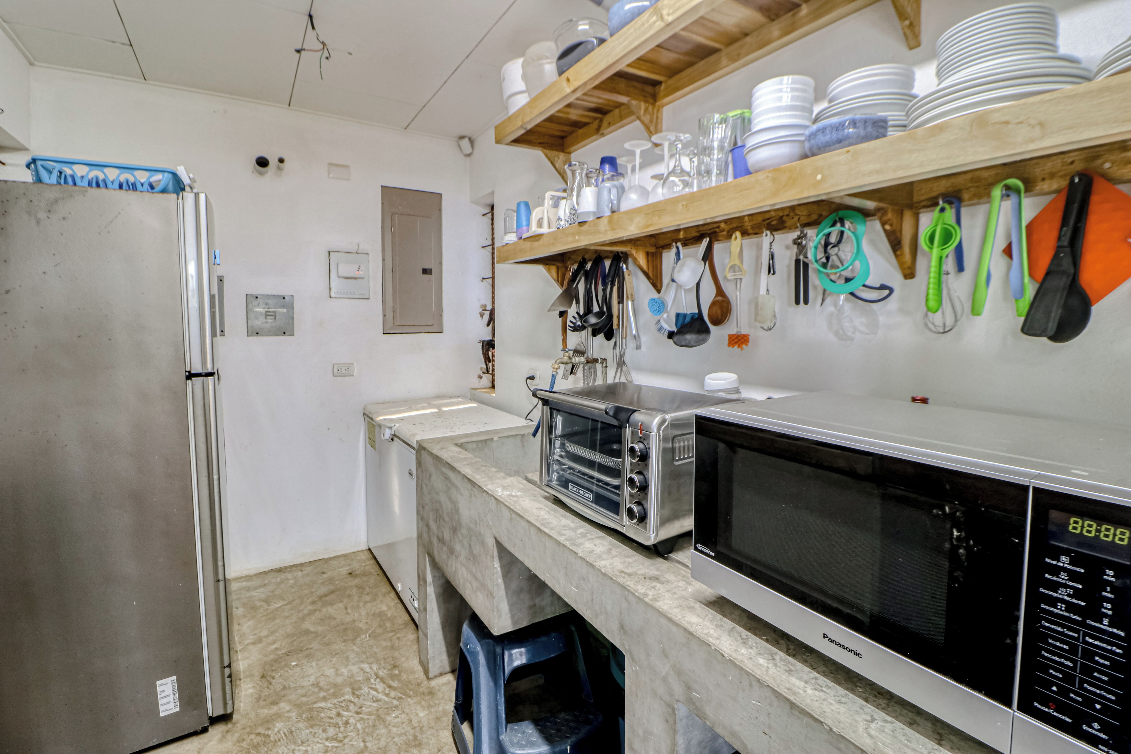 A kitchen with a stainless steel refrigerator, a microwave, and a toaster oven. There are shelves above the counter holding dishes and utensils.