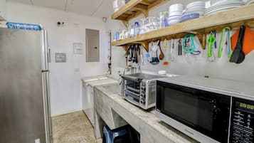 A kitchen with a stainless steel refrigerator, a microwave, and a toaster oven. There are shelves above the counter holding dishes and utensils.