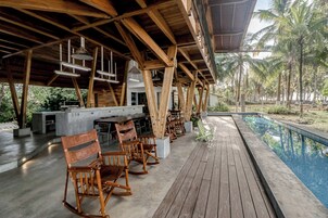 An outdoor seating area with wooden furniture, a pool, and a view of palm trees.
