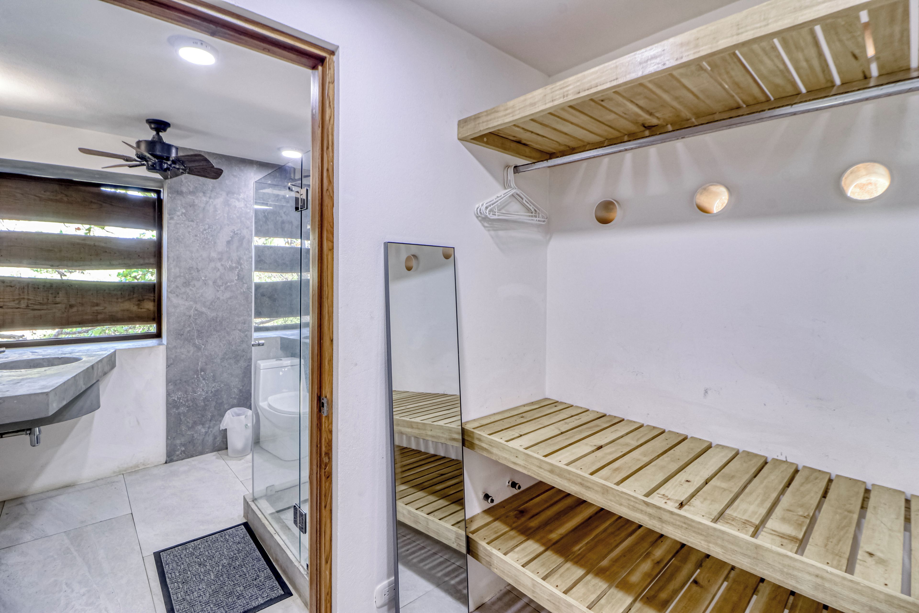 A bathroom with a glass shower enclosure, a wooden shelf unit, and a marble-tiled floor.