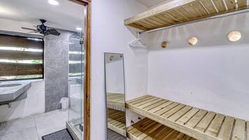 A bathroom with a glass shower enclosure, a wooden shelf unit, and a marble-tiled floor.