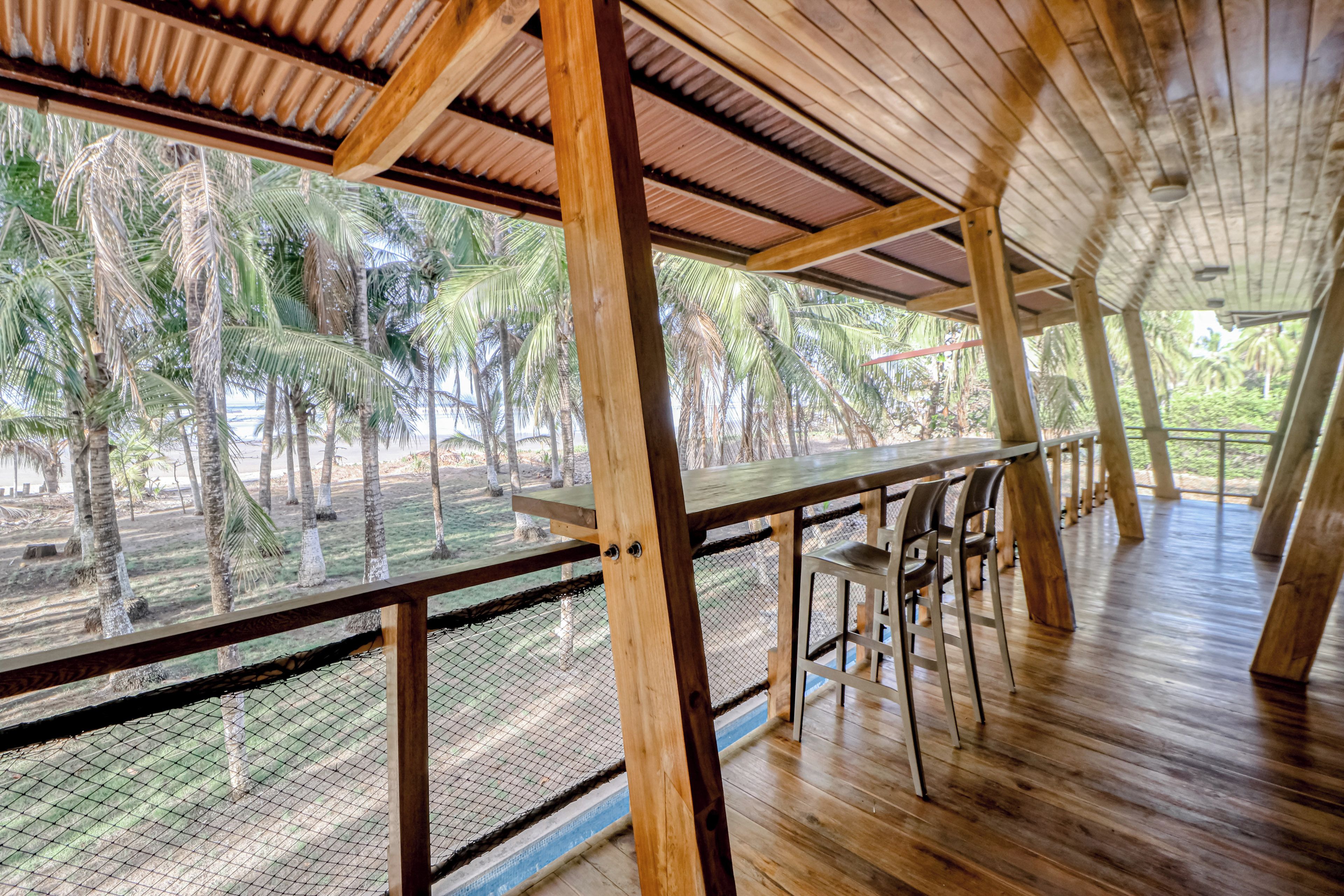 A wooden deck with a table and chairs, overlooking a tropical landscape with palm trees.