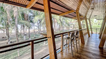A wooden deck with a table and chairs, overlooking a tropical landscape with palm trees.