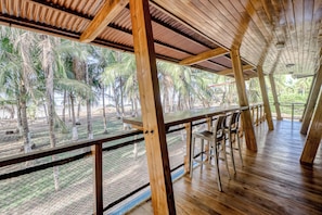 A wooden deck with a table and chairs, overlooking a tropical landscape with palm trees.