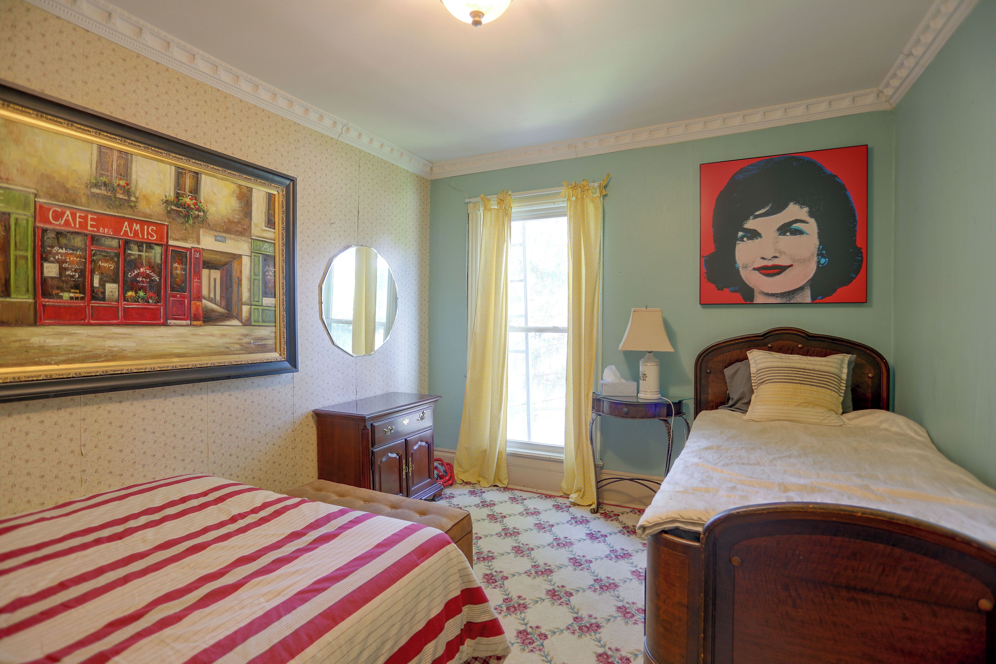 A bedroom with two beds, a dresser, a mirror, a window with curtains, and a painting on the wall.