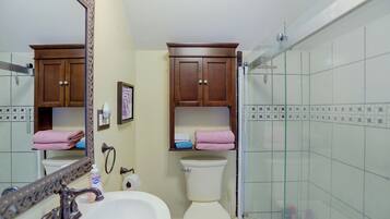 A bathroom with a white sink, a toilet, a shower with glass doors, and wooden cabinets above the toilet.
