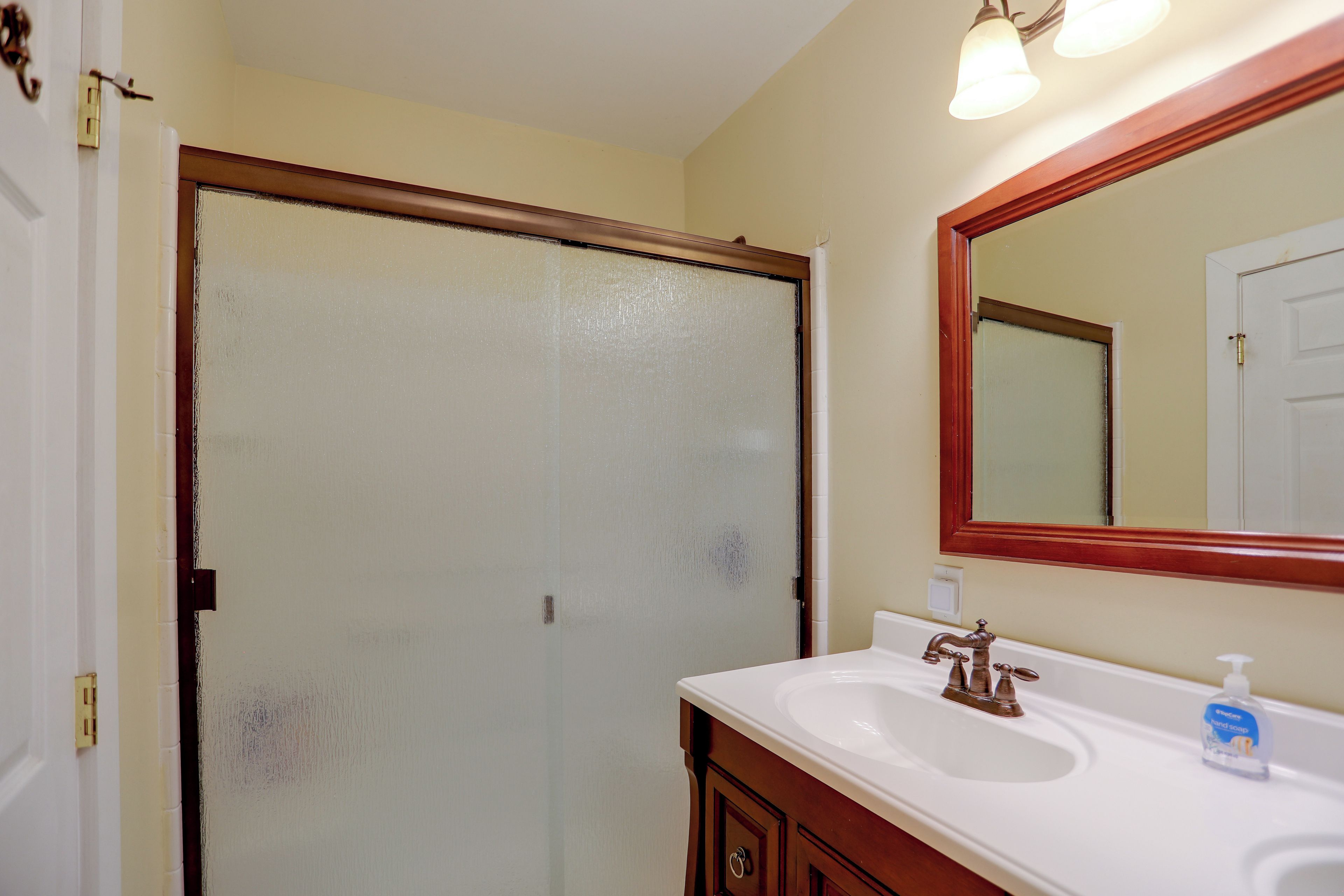 A bathroom with a white sink, a mirror, and a frosted glass door.