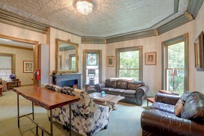 A room with a fireplace, leather sofa, floral patterned ottoman, and large windows with framed pictures. - Downtown Spacious 5BR w/ Game Room (Ellicottville)