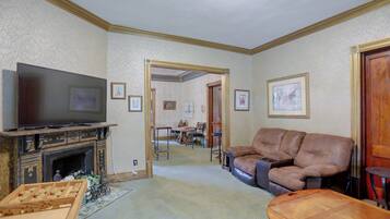 A living room with a television, a fireplace, a sofa, and a dining area in the background.