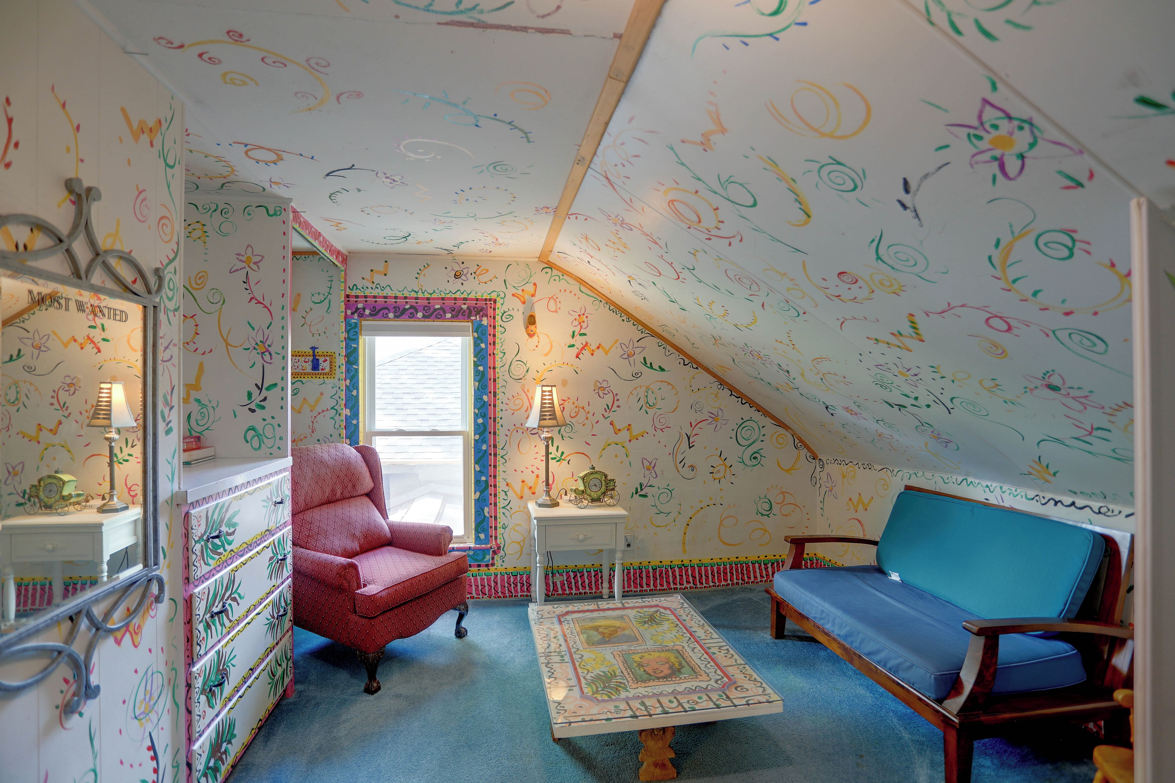 A cozy attic room with a sloped ceiling, a red armchair, a blue sofa, and a patterned rug.