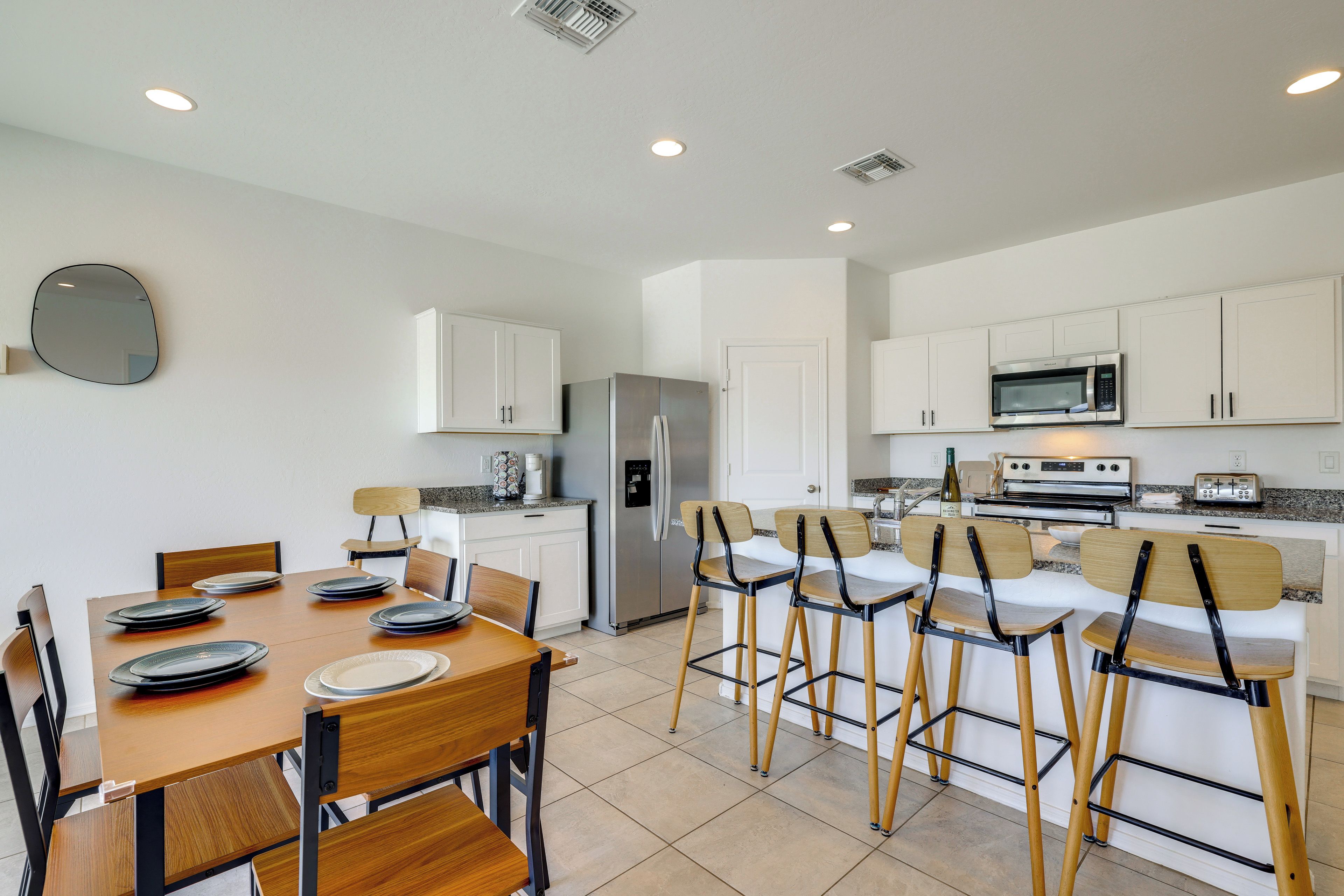 A modern kitchen with white cabinets, stainless steel appliances, and a dining area with wooden chairs and plates.