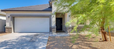 A residential house with a garage, a stone entrance, and a tree in the front yard.