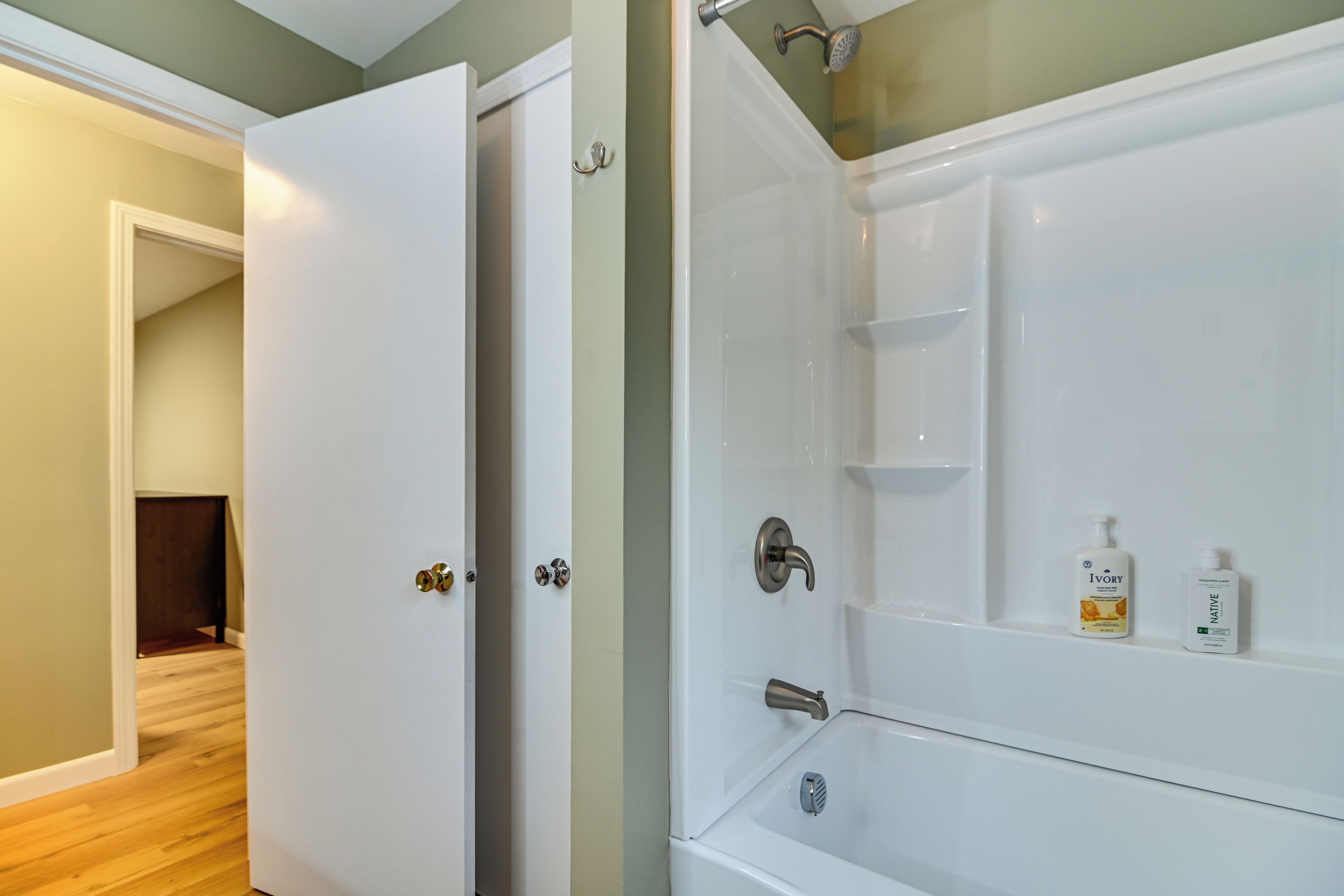 A bathroom with a white bathtub, a shower, and a door leading to another room.