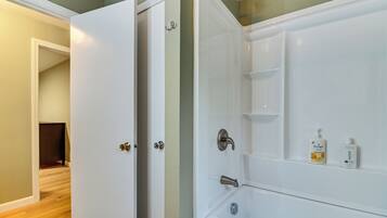 A bathroom with a white bathtub, a shower, and a door leading to another room.