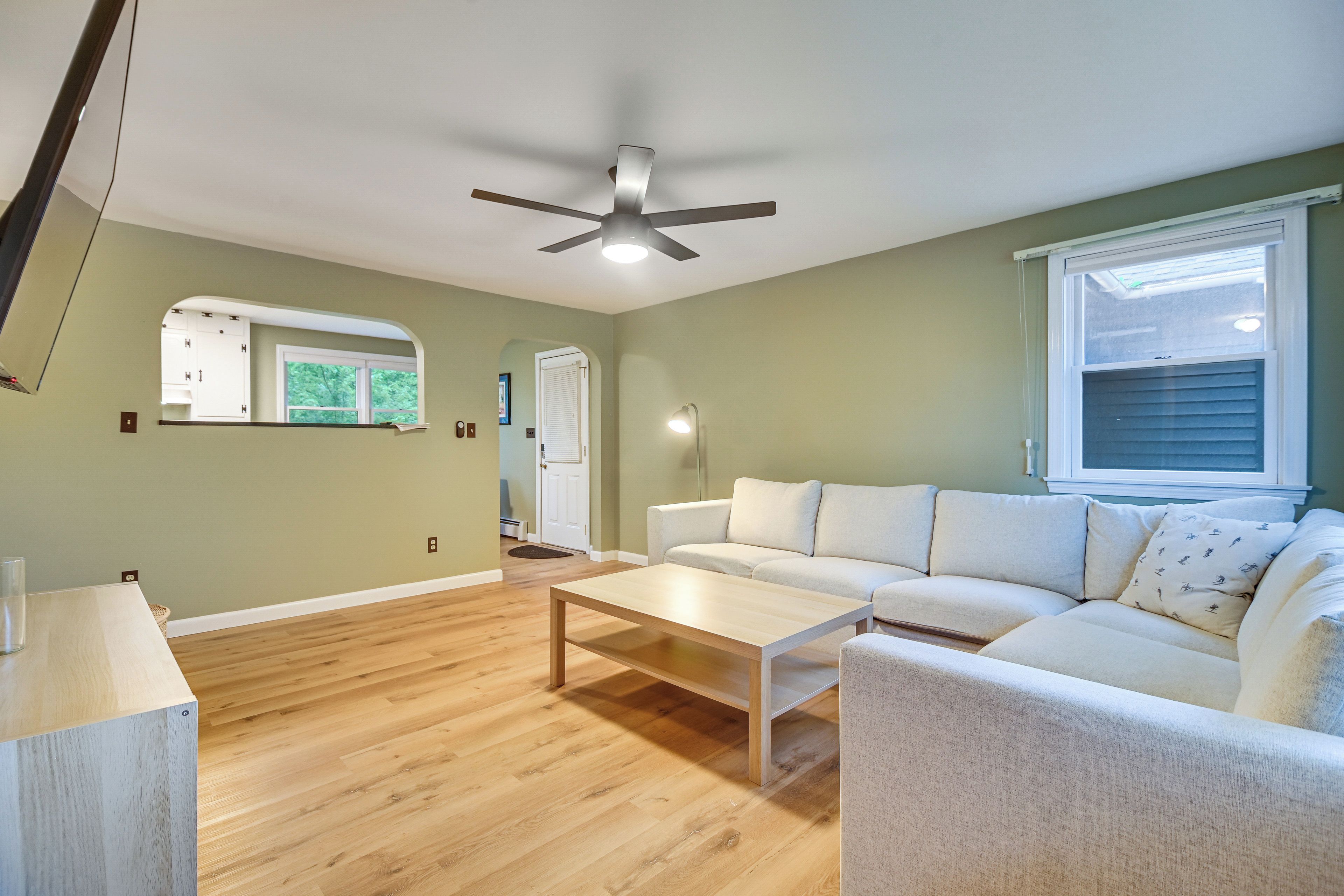 A living room with a ceiling fan, a white sofa, a wooden coffee table, and a window with blinds.