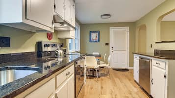 A kitchen with a granite countertop, white cabinets, a dining area with a table and chairs, and a door with a window.