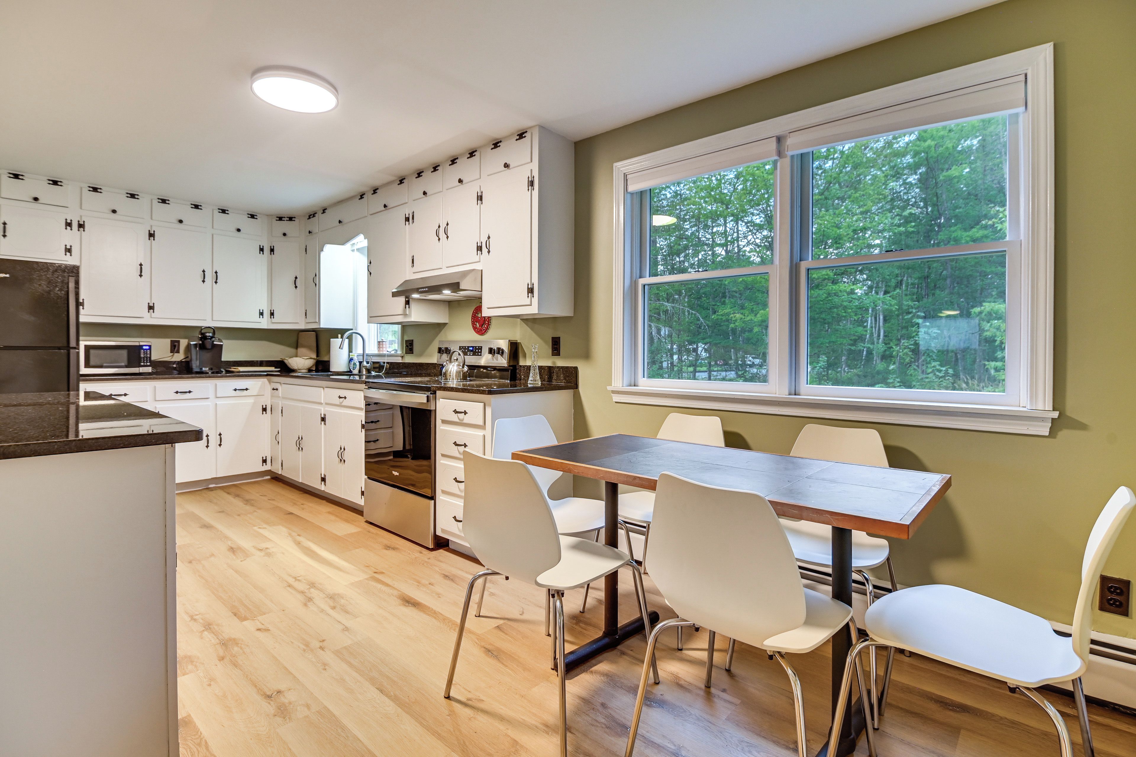 A modern kitchen with white cabinets, stainless steel appliances, and a dining area with a table and chairs.