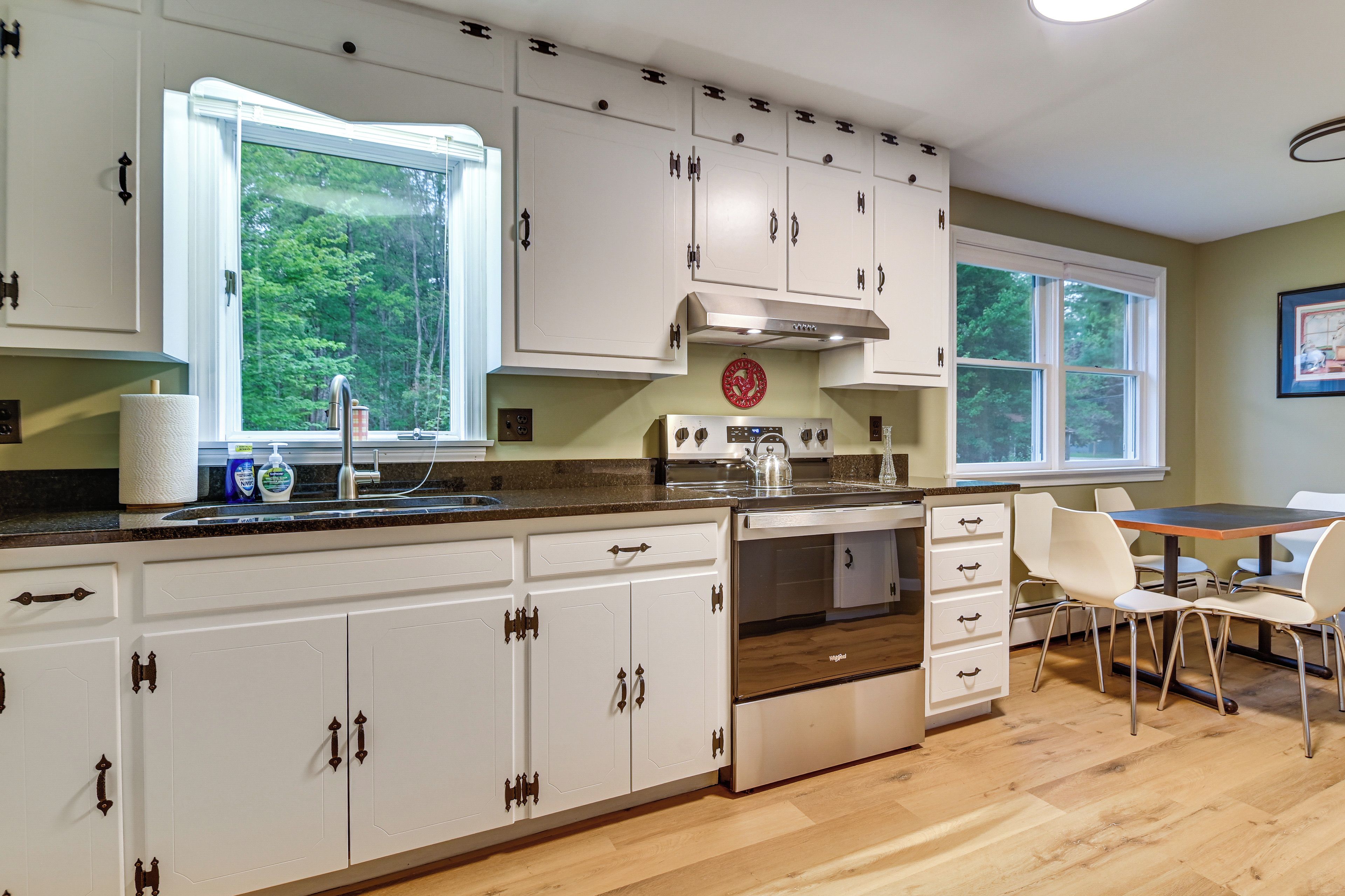 A kitchen with white cabinets, a stove, and a dining area with a table and chairs.